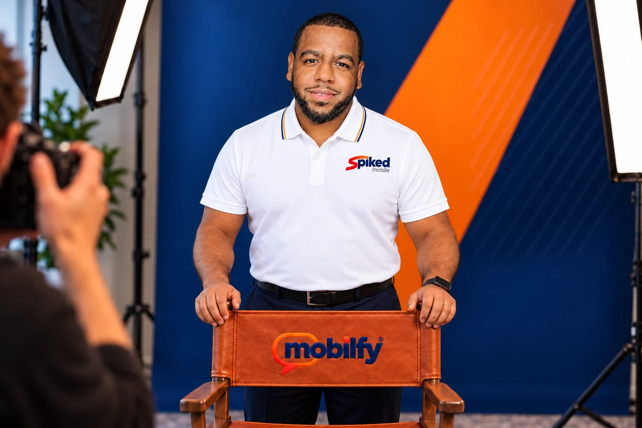 Darnel Wiltshire in a studio portrait, standing behind a leather director’s chair embroidered with the Mobilfy logo