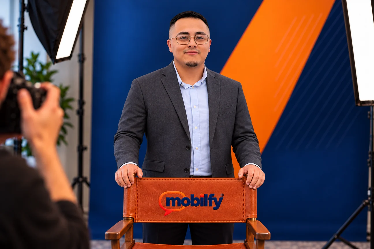 Jacob Perez in a studio portrait, standing behind a leather director’s chair embroidered with the Mobilfy logo