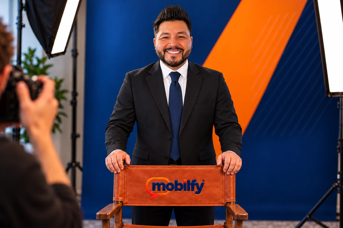 Laurence Perez in a studio portrait, standing behind a leather director’s chair embroidered with the Mobilfy logo