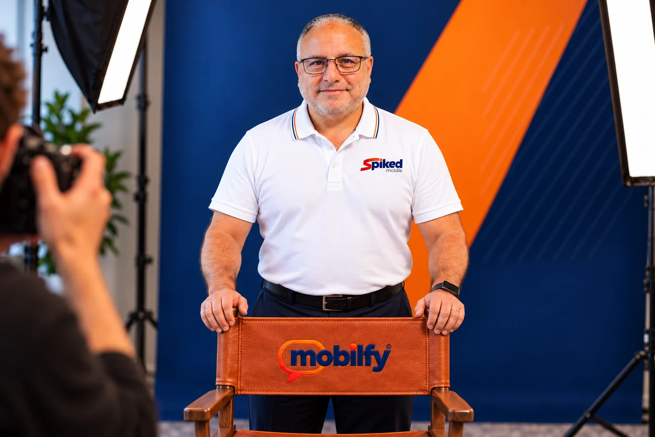 Tom Salvato in a studio portrait, standing behind a leather director’s chair embroidered with the Mobilfy logo